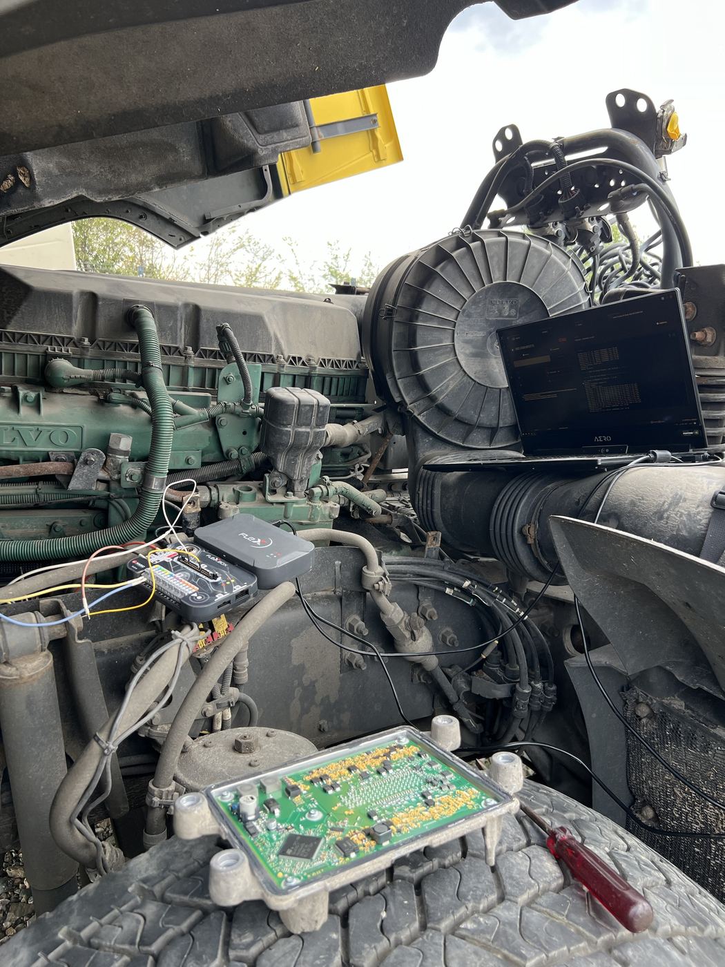 Opened truck ECU circuit board resting on a tyre next to the engine